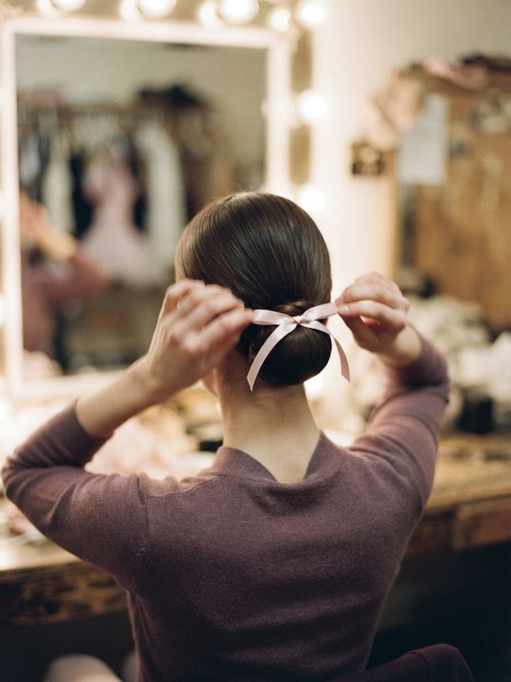 Dancer tying a satin bow into her bun backstage